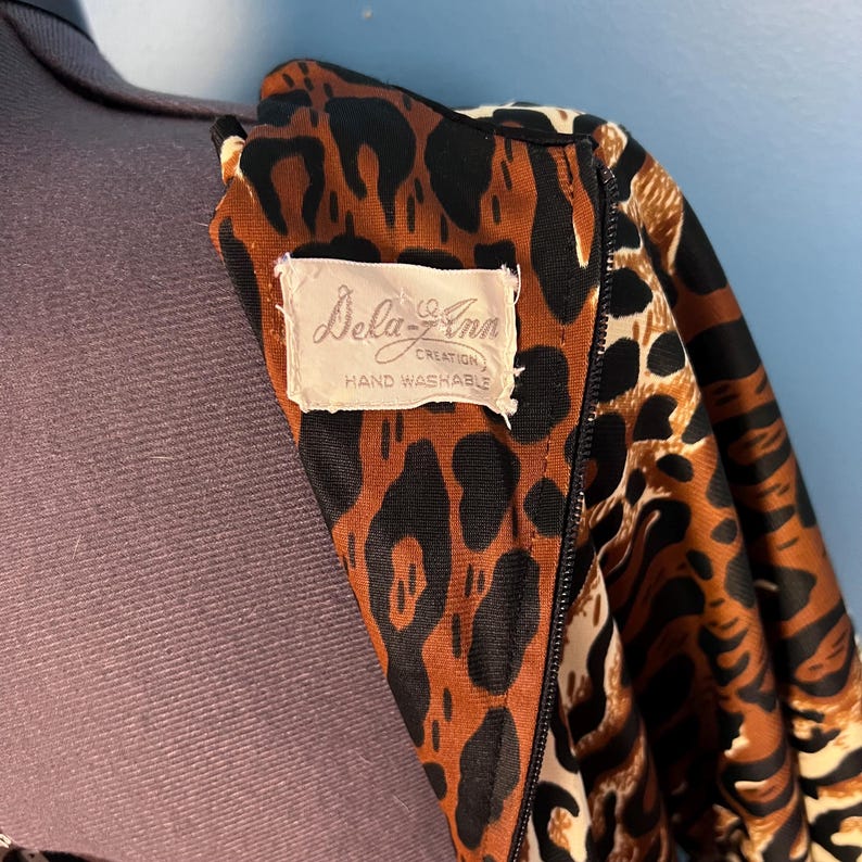 Puede incluir: Primer plano de una tela de estampado de leopardo marr&oacute;n y negro con una etiqueta blanca que dice "Dela-Z-Ann Creation Hand Washable".
