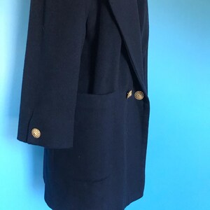 Pu&ograve; includere: Un cappotto blu scuro a maniche lunghe con una sola tasca sul lato sinistro e due bottoni dorati sul lato destro.