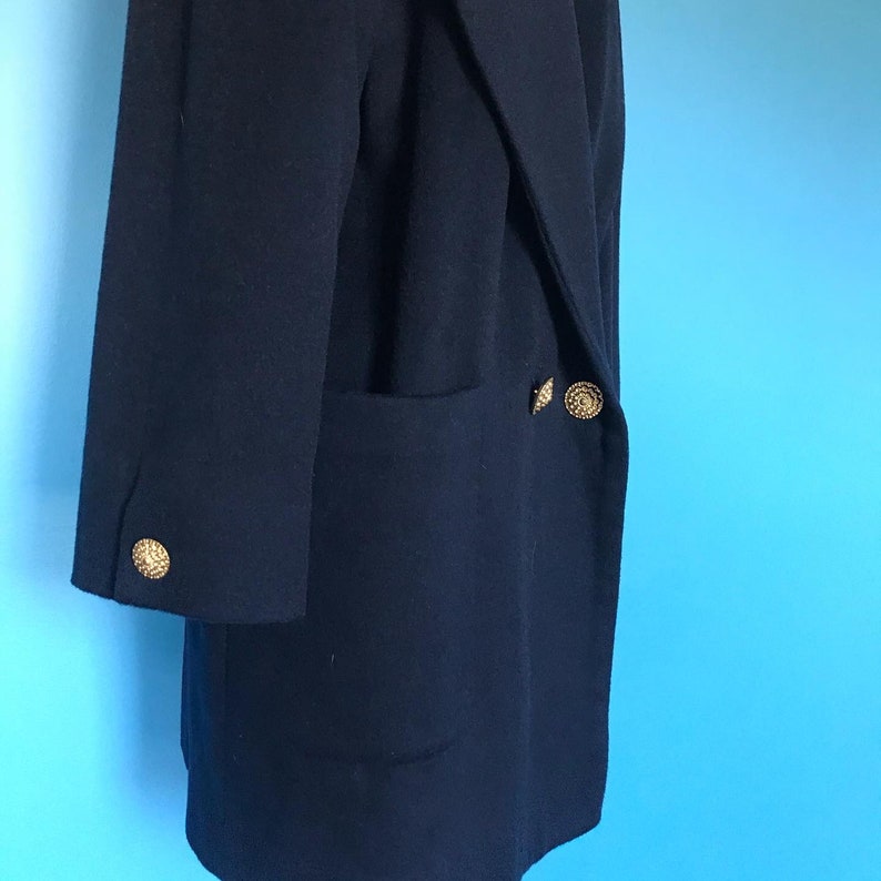 Pu&ograve; includere: Un cappotto blu scuro a maniche lunghe con una sola tasca sul lato sinistro e due bottoni dorati sul lato destro.