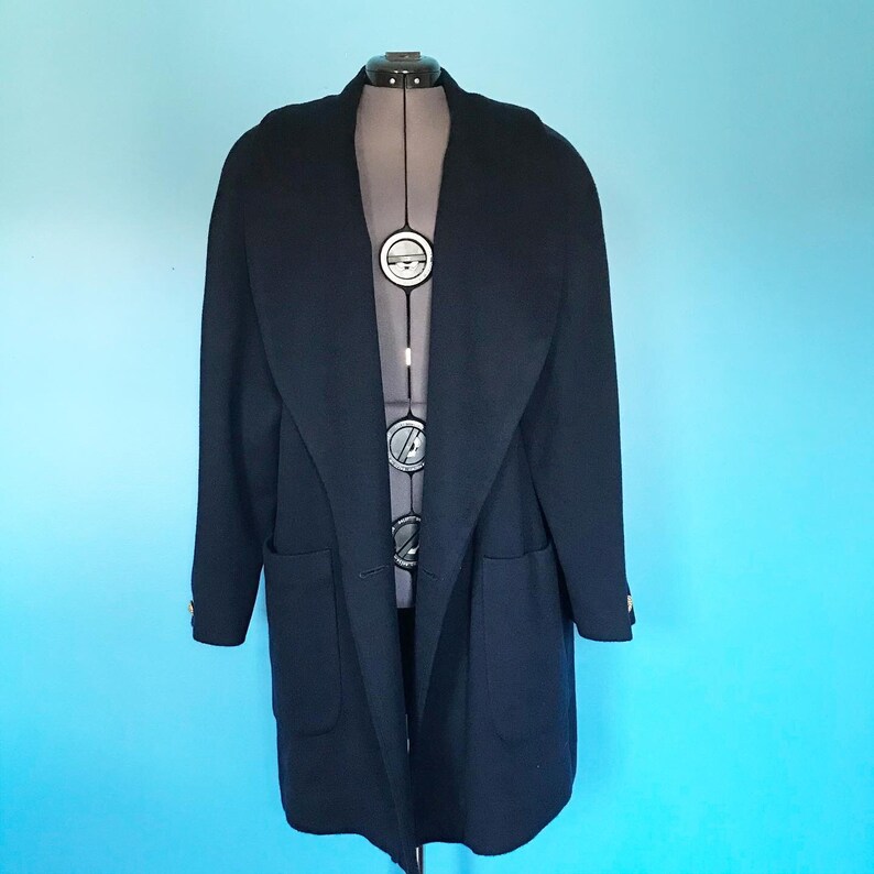 Pu&ograve; includere: Un lungo cappotto di lana blu navy con un ampio colletto e due tasche. Il cappotto ha una chiusura con un solo bottone e bottoni dorati.