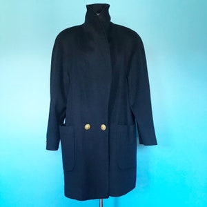 Pu&ograve; includere: Un lungo cappotto blu scuro con collo alto e due bottoni dorati. Il cappotto ha due grandi tasche sul davanti.