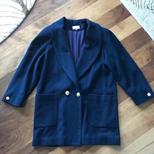 Pu&ograve; includere: Un cappotto blu navy doppiopetto con un ampio colletto e bottoni dorati. Il cappotto ha due grandi tasche sul davanti.