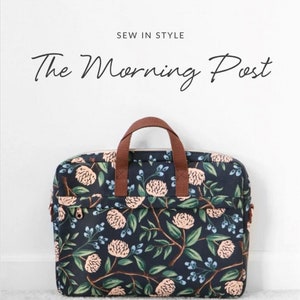 May include: A black laptop bag with a floral print featuring pink flowers and green leaves. The bag has brown handles and a zipper closure. The text "The Morning Post" is written in black cursive above the bag. The text "Sallie Tomato" is written in black cursive below the bag. The text "Your source for quality sewing patterns & supplies" is written in black below the logo.