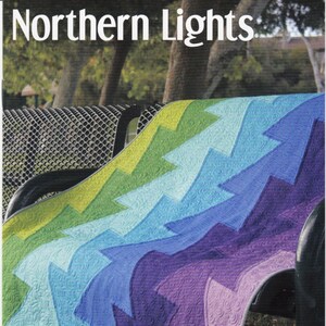 May include: A colorful quilt with a zig-zag pattern in shades of green, blue, and purple. The quilt is draped over a bench and the text "Northern Lights" and "JAYBIRD QUILTS" is visible.