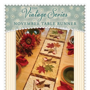 May include: A quilted table runner featuring a fall theme with birds and leaves in shades of red, orange, green, and brown. The table runner is made up of five squares and is displayed on a wooden table with a sunflower centerpiece. The text "The Vintage Series November Table Runner" is at the top of the image. The text "Shabby Fabrics.com" is at the bottom of the image.