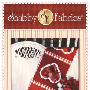 May include: A red and white patchwork Valentine's Day table runner with three white hearts with scalloped edges. The table runner is draped over a white wicker chair. The text "Patchwork Valentine Table Runner" is at the bottom of the image.