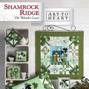 May include: A green and white quilt with a shamrock design. The quilt is displayed on a wooden table with a pillow and other decorative items. The quilt is titled "Shamrock Ridge" and the text "Art to Heart" is displayed on a sign above the quilt.