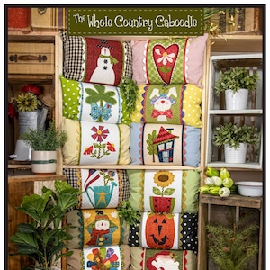 May include: A collection of 12 pillow covers with various country-themed designs, including a snowman, a heart, a shamrock, a bunny, a flower, a house, a watering can, a sunflower, a scarecrow, a pumpkin, a turkey, and Santa Claus. The pillow covers are arranged in a wooden crate. The text "The Whole Country Caboodle" and "Wrapped in Love" are visible on the image. The pillow covers are 13 inches by 18 1/2 inches and the pillow wraps are 9 inches by 30 inches.