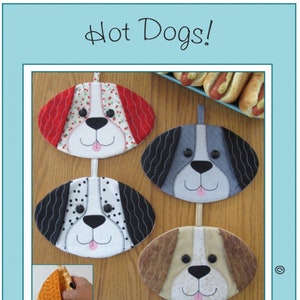 May include: Four fabric hot pads shaped like dog faces. The hot pads are in red, gray, black and white, and brown. The hot pads are hanging from a wooden surface. The text "Hot Dogs!" is at the top of the image. The text "Susie C Shore Designs" is at the bottom of the image.