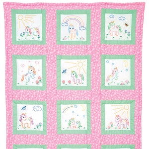 May include: A pink and green quilt with nine embroidered squares featuring different unicorn designs. Each square has a white background with a green border and a pink background.