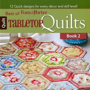 May include: A book titled "Best of Fons & Porter Tabletop Quilts Book 2" featuring a colorful quilt with a hexagonal pattern. The quilt is made with floral fabric in shades of red, pink, yellow, blue, and green.