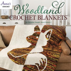 May include: A book cover featuring a crocheted blanket with a woodland animal design. The title is "Woodland Crochet Blankets" by Christine Naugle, Sweet Potato 3. The book features 6 whimsical designs.