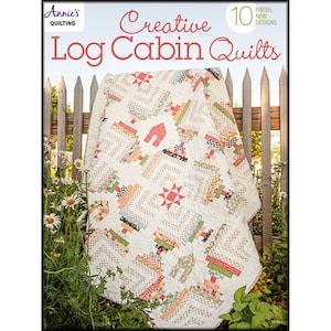 May include: A quilt book titled "Creative Log Cabin Quilts" with a cream-colored quilt draped over a wooden fence. The quilt features log cabin blocks in various colors and patterns, including red, green, and beige. The book cover has text that reads "Annie's Quilting".