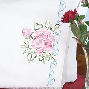 May include: White pillowcase with a blue and white embroidered border and a pink and green embroidered rose design.