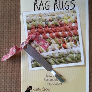 May include: A guide for making rag rugs, with a photo of a colorful rug and a tool for weaving. The guide is titled "Rag Rugs" and includes the text "Easy, Detailed Rectangular Rug Instructions". The guide is from "Rusty Crow Quilt Shop".