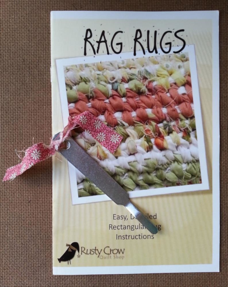 May include: A guide for making rag rugs, with a photo of a colorful rug and a tool for weaving. The guide is titled "Rag Rugs" and includes the text "Easy, Detailed Rectangular Rug Instructions". The guide is from "Rusty Crow Quilt Shop".