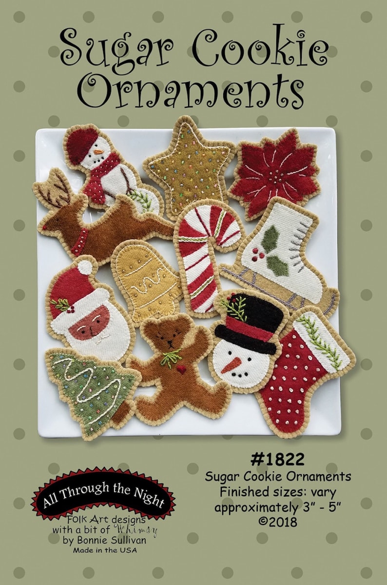 May include: A set of 12 felt ornaments shaped like Christmas cookies, including a snowman, reindeer, gingerbread man, candy cane, and stocking. The ornaments are on a white plate and have a rustic, handmade look. The text "Sugar Cookie Ornaments" and "All Through the Night" is visible on the image. The ornaments are approximately 3 to 5 inches in size.