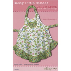 May include: A sewing pattern for a child's apron with a floral print and green polka dots. The pattern is called "Sassy Little Sisters Child's Apron" and includes three sizes: small, medium, and large. The pattern is from Cabbage Rose.