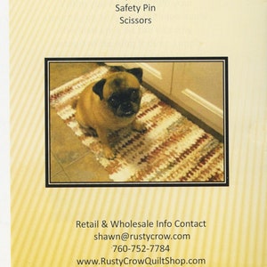 May include: A close-up of a brown and white rug with a pug dog sitting on it. The rug is made of braided fabric and has a striped pattern. The text "Supplies Needed: Fabric (6 yards needed to make a 17" x 24" rug) Tool (Included) Safety Pin Scissors" is printed on the back of the rug.