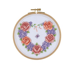 May include: A white embroidery hoop with a heart-shaped design of pink and orange roses and purple flowers.