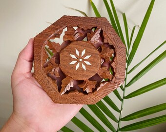 May include: A wooden coaster with intricate carvings and a white star design in the center. The coaster is octagonal in shape and has a dark brown color.