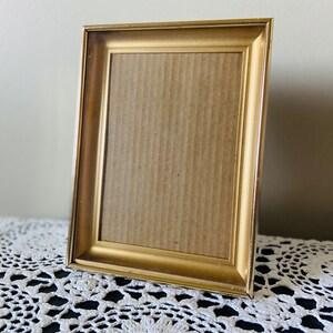 May include: A gold-colored picture frame with a simple design. The frame is empty and ready to hold a photo or artwork.