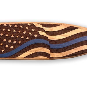 May include: Wooden paddle with a carved American flag design. The flag features stars, stripes, and a blue line. The paddle is made of light-colored wood with a dark wood flag design.