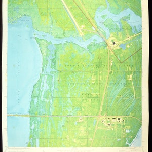 May include: A vintage topographic map of the John F. Kennedy Space Center and Merritt Island National Wildlife Refuge in Florida. The map features detailed land and water features, including the Banana River and Indian River. The map is printed in shades of green, blue, and tan.