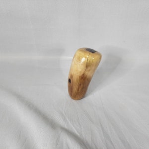 May include: A wooden gear shift knob with a natural wood finish and a dark brown center.
