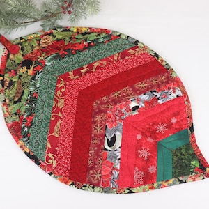 May include: A quilted Christmas tree skirt in the shape of a leaf, featuring a patchwork design of red, green, and gold fabrics with various holiday patterns.
