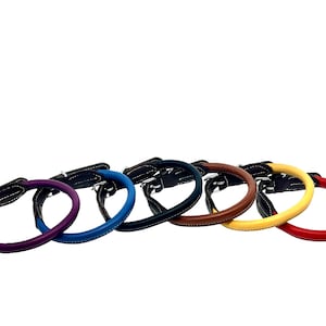May include: Six leather dog collars in different colors: purple, blue, black, brown, yellow, and red. The collars are all made of the same type of leather and have a similar design.