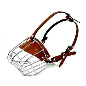 May include: A brown leather dog muzzle with a chrome wire cage. The muzzle has adjustable straps with buckles.