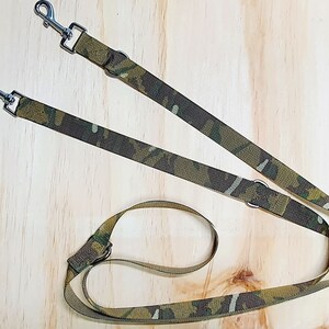 Puede incluir: Correa para perros con estampado de camuflaje con dos mosquetones metálicos y un lazo. La correa presenta un diseño de camuflaje verde, marrón y beige. Diseñada para pasear a dos perros a la vez.
