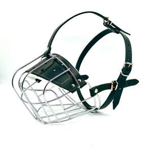May include: A black leather dog muzzle with a chrome wire cage. The muzzle has adjustable straps with buckles.