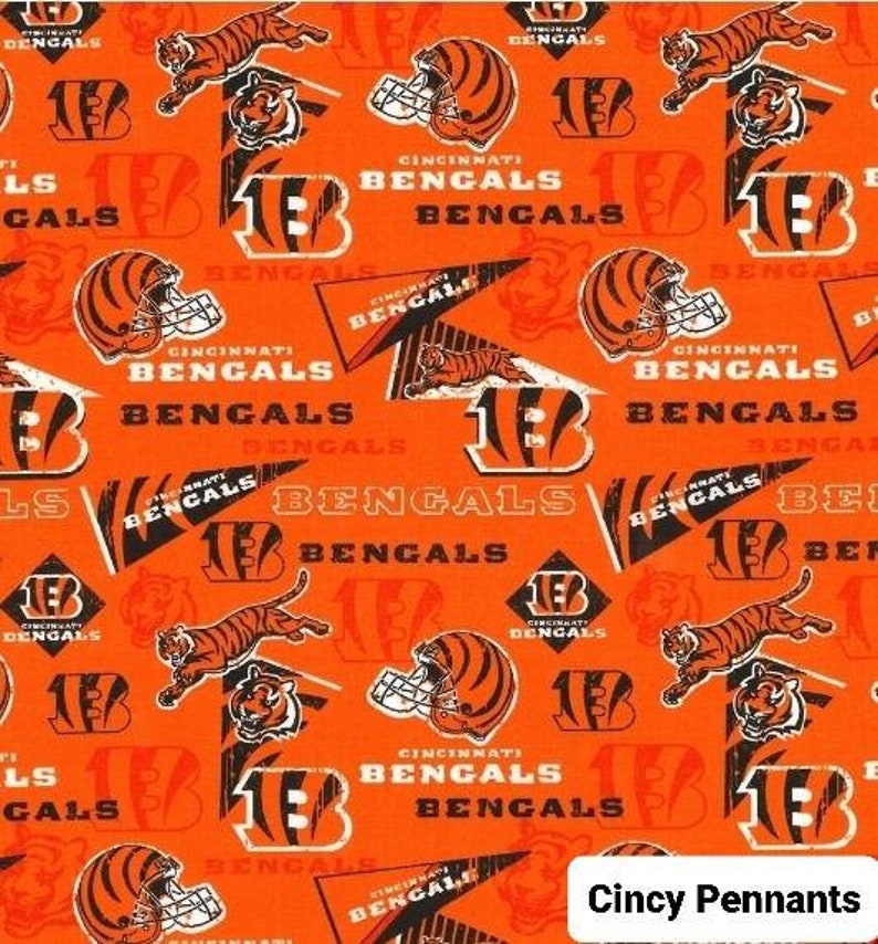 May include: Orange fabric with a repeating pattern of black and white Cincinnati Bengals logos, including the team's mascot, a tiger, and the words "Cincinnati Bengals". The fabric also features pennant flags with the words "Cincy Pennants".