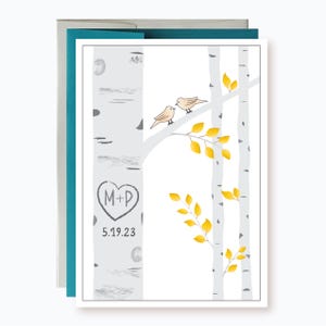 May include: A white card with a birch tree design featuring two birds perched on a branch with yellow leaves. The tree trunk has a heart with the initials "M+P" and the date "5.19.23". The card is layered with teal and gray backing.