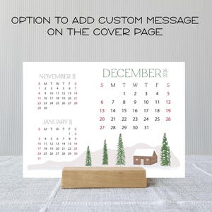 May include: A desk calendar with the months of November, December, and January displayed. The calendar features a winter scene with trees and a cabin. The text "OPTION TO ADD CUSTOM MESSAGE ON THE COVER PAGE" is at the top.