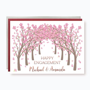 May include: Engagement card featuring a floral archway of pink cherry blossoms. The words "Happy Engagement" and the names "Michael & Amanda" are written in a copper-colored script on a white background.