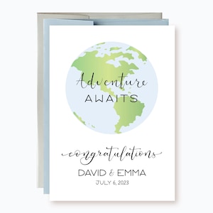 May include: A white card with a green and blue globe illustration. The text "Adventure Awaits" is written in black cursive font above the globe. Below the globe, the text "congratulations DAVID & EMMA JULY 6, 2023" is written in black cursive font.
