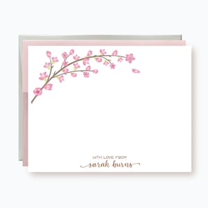 May include: A white card with a pink and green cherry blossom branch design in the upper left corner. The text "WITH LOVE FROM sarah burns" is printed in brown cursive at the bottom of the card.