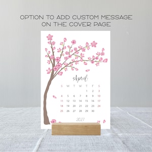 May include: A 2027 calendar page for April featuring a brown tree branch with pink cherry blossoms. The text reads OPTION TO ADD CUSTOM MESSAGE ON THE COVER PAGE, April, and 2027. The calendar grid displays dates from 1 to 30 in black and red.