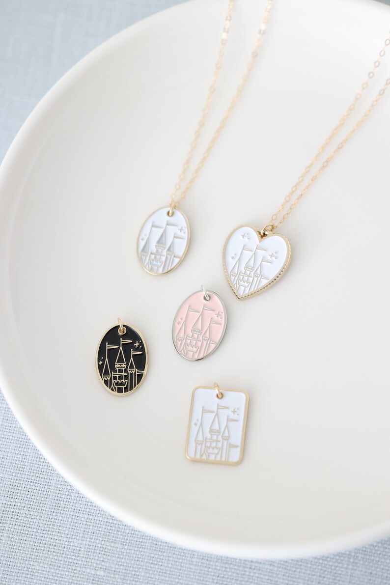 May include: Four gold necklaces with different pendant shapes featuring a white castle design. The pendants are a circle, a heart, a square, and a circle with a black background.