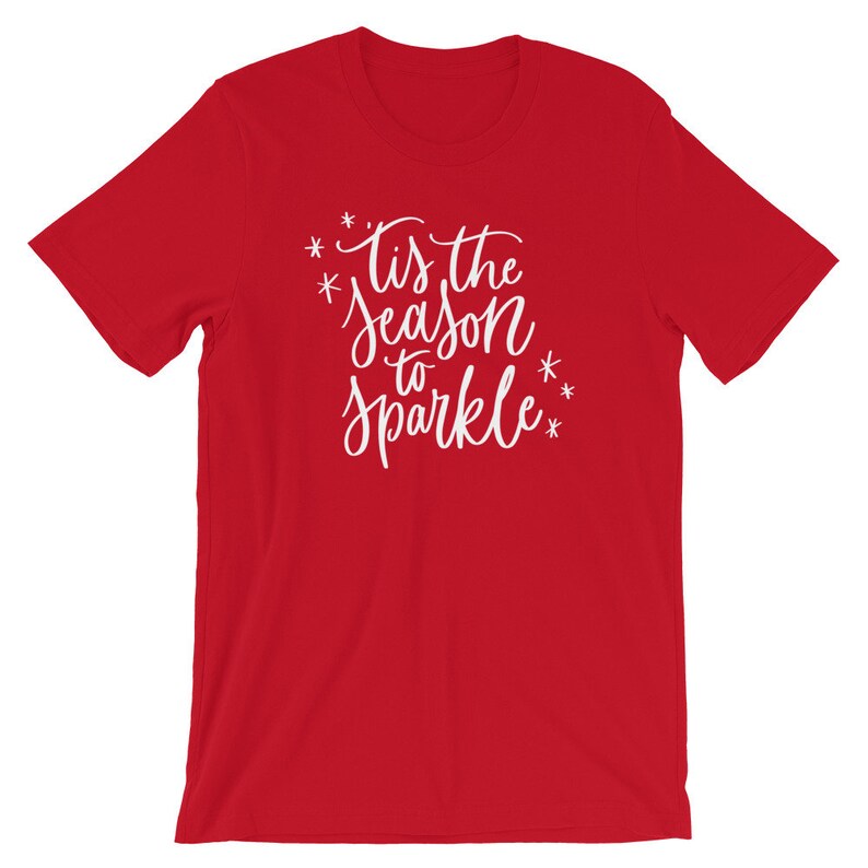 May include: Red short-sleeved t-shirt with white text that reads "*Tis the season to sparkle*" with stars around the text.