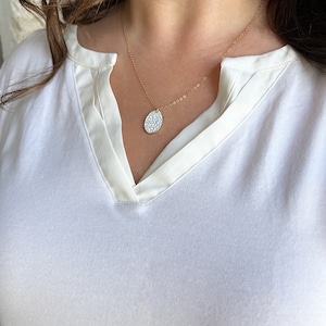 May include: A gold chain necklace with a white oval pendant featuring a delicate floral pattern. The necklace is 20 inches long.