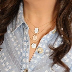 May include: Three gold necklaces of varying lengths, 16, 18, and 20 inches, each with a different pendant. The pendants feature engraved designs of a cowboy boot, a cowboy boot, and a cloud with stars. The necklaces are displayed against a light blue floral shirt.