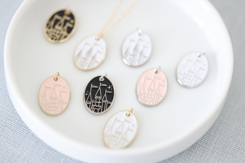 May include: A set of eight oval-shaped pendants featuring a stylized castle design. The pendants are in various colors, including black, white, pink, and silver.