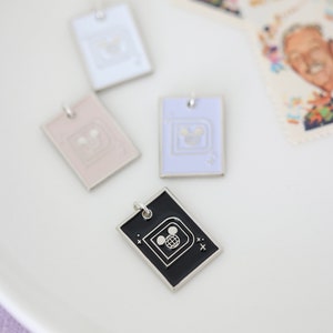 May include: Four rectangular pendant necklaces in white, pink, lavender, and black, each with a silver border and a Disney-themed design. The black pendant features a Mickey Mouse globe design. Stamps with a man's portrait are in the background.