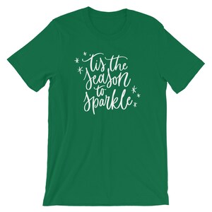 May include: Green t-shirt with white text that reads "Tis the season to sparkle" with stars around the text.