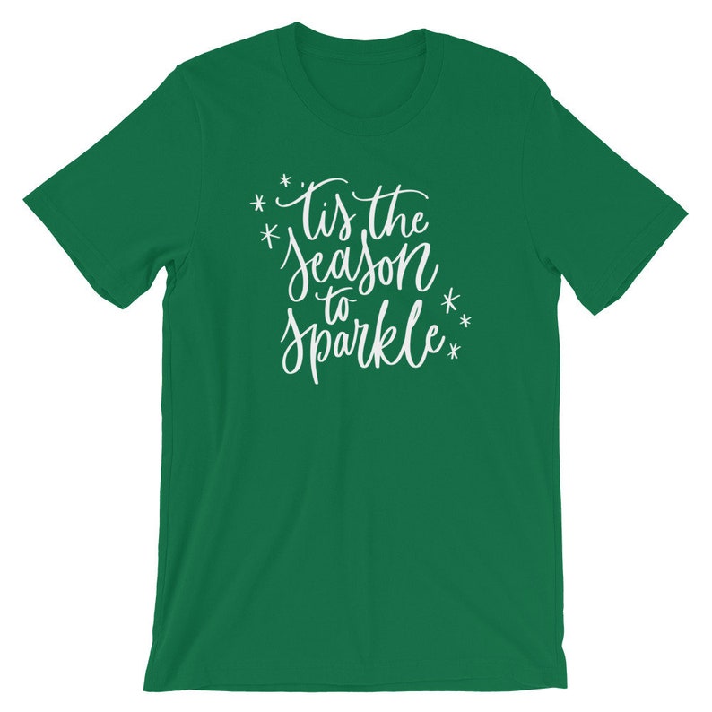 May include: Green t-shirt with white text that reads "Tis the season to sparkle" with stars around the text.