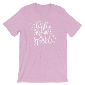 May include: A light pink t-shirt with the text "Tis the season to sparkle" in white lettering.